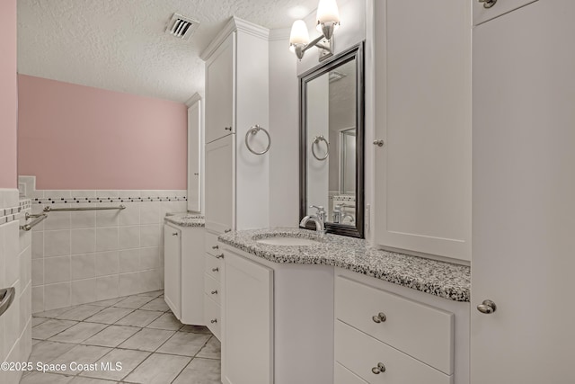 bathroom featuring a textured ceiling, vanity, wainscoting, tile patterned flooring, and tile walls