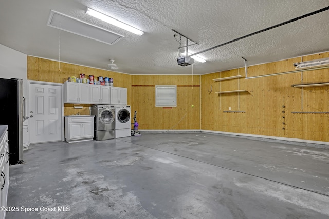 garage with a garage door opener, washing machine and clothes dryer, freestanding refrigerator, and wood walls