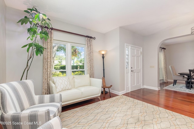 living area with arched walkways, baseboards, and wood finished floors