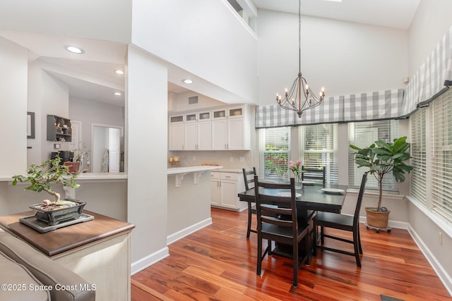 dining area with baseboards, a chandelier, wood finished floors, and a towering ceiling