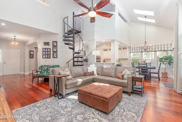 living area with a high ceiling, ceiling fan with notable chandelier, stairs, baseboards, and wood finished floors