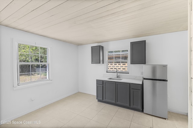 kitchen featuring gray cabinets, light countertops, a sink, freestanding refrigerator, and baseboards