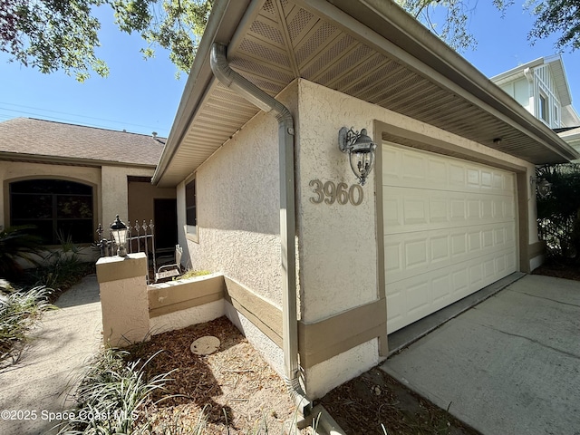 view of side of home featuring an attached garage, concrete driveway, and stucco siding