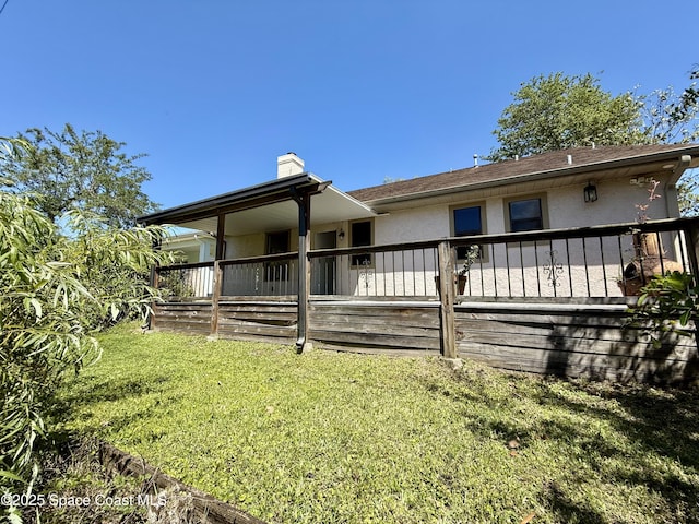 rear view of house featuring a chimney, stucco siding, a deck, and a lawn