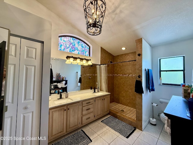 bathroom with a sink, a textured ceiling, double vanity, tiled shower, and tile patterned flooring