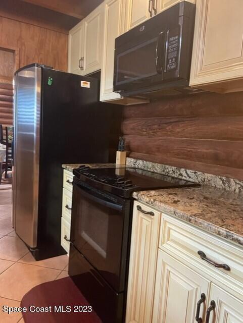 kitchen with black appliances, cream cabinetry, light tile patterned floors, and light stone counters