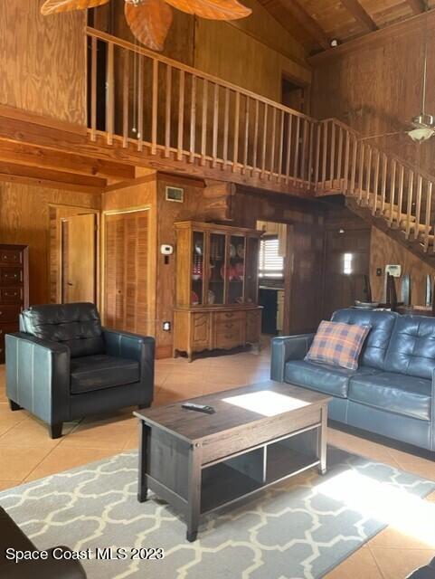 tiled living area featuring high vaulted ceiling, visible vents, and wooden walls