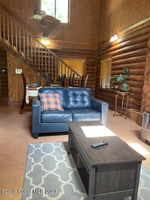 living room featuring light tile patterned flooring, stairs, a high ceiling, and log walls