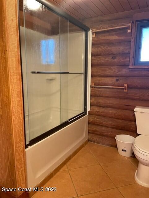 bathroom featuring log walls, toilet, enclosed tub / shower combo, tile patterned flooring, and wood ceiling