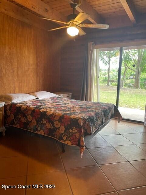 bedroom with light tile patterned floors, wood ceiling, access to exterior, beamed ceiling, and wooden walls