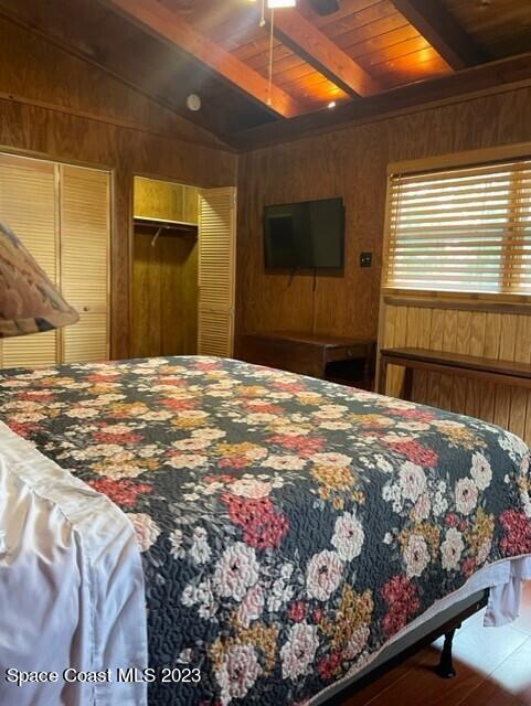 bedroom with vaulted ceiling with beams, wooden walls, and wooden ceiling