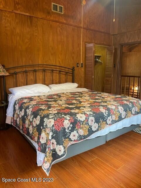 bedroom featuring visible vents, a closet, wood finished floors, and wooden walls