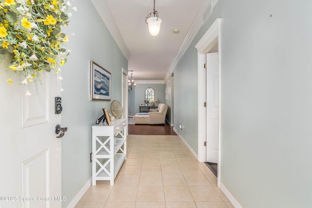 corridor with baseboards, a chandelier, light tile patterned floors, crown molding, and visible vents