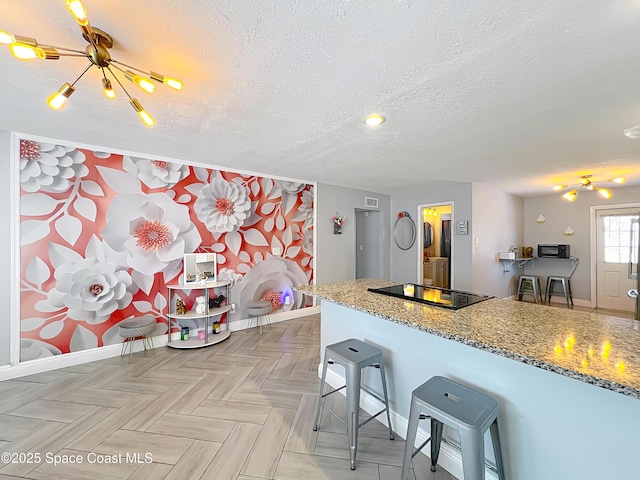 1760 Tee Dee Ln, Titusville, FL 32780 - kitchen featuring a textured ceiling, black electric cooktop, a chandelier, light stone countertops, and a breakfast bar area