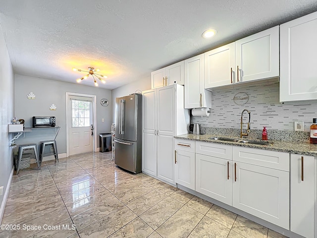 1760 Tee Dee Ln, Titusville, FL 32780 - kitchen with a sink, freestanding refrigerator, stone countertops, white cabinets, and decorative backsplash