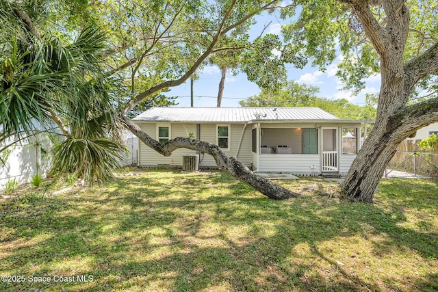 single story home with cooling unit, a sunroom, fence, metal roof, and a front yard
