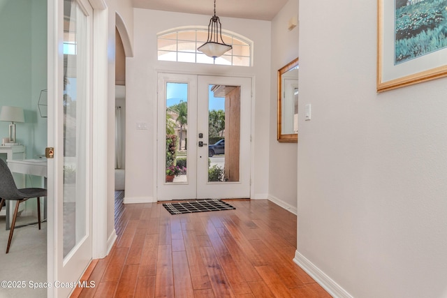 entryway featuring arched walkways, wood-type flooring, french doors, and baseboards