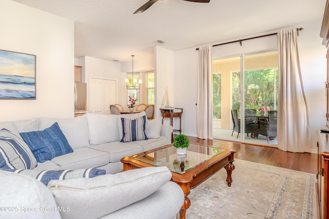 living room with visible vents, baseboards, wood finished floors, and ceiling fan with notable chandelier