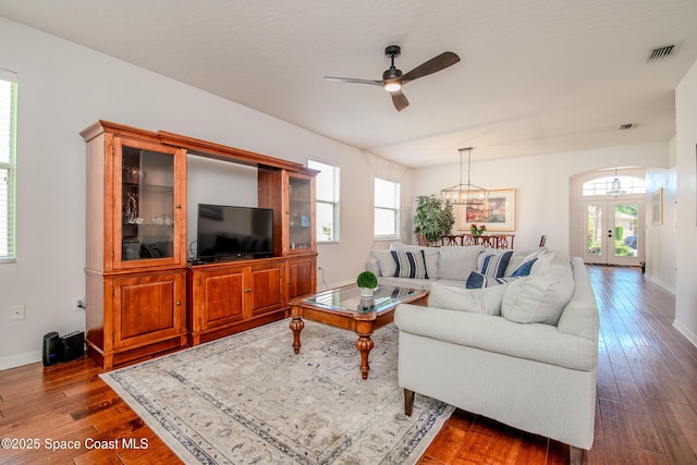 living room featuring french doors, a healthy amount of sunlight, ceiling fan with notable chandelier, and dark wood-style floors