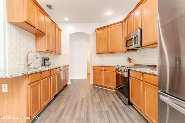 kitchen with arched walkways, a sink, stainless steel appliances, light wood finished floors, and backsplash