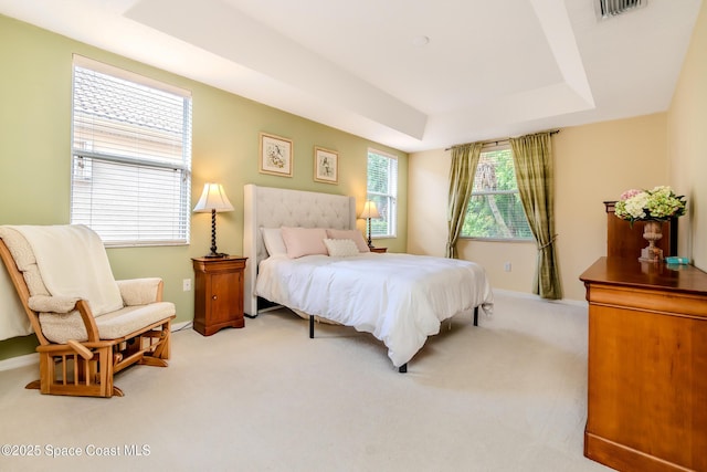 bedroom featuring light carpet, visible vents, baseboards, and a raised ceiling
