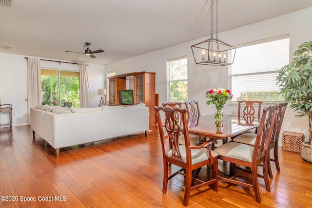 dining space with a textured ceiling, light wood-type flooring, a wealth of natural light, and ceiling fan with notable chandelier