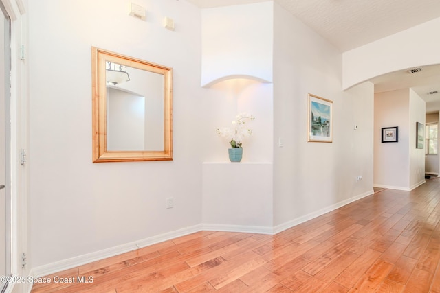 corridor with light wood-style floors, visible vents, and baseboards