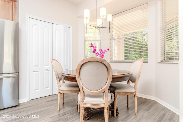 dining room with light wood-style flooring, baseboards, and an inviting chandelier