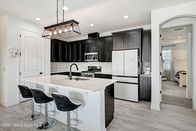 kitchen featuring decorative light fixtures, dark cabinetry, stainless steel appliances, a sink, and light stone countertops