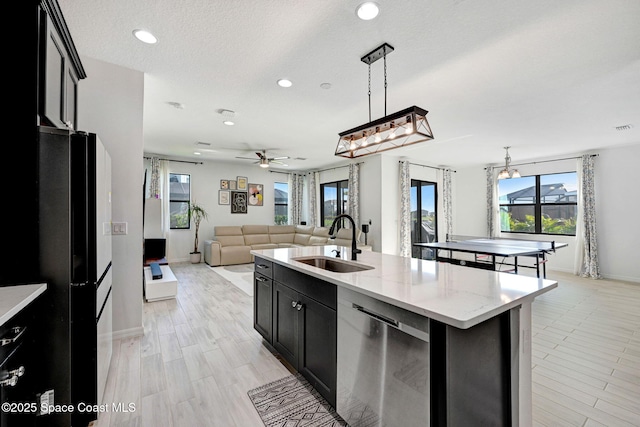 kitchen featuring dishwasher, ceiling fan, a sink, dark cabinets, and open floor plan