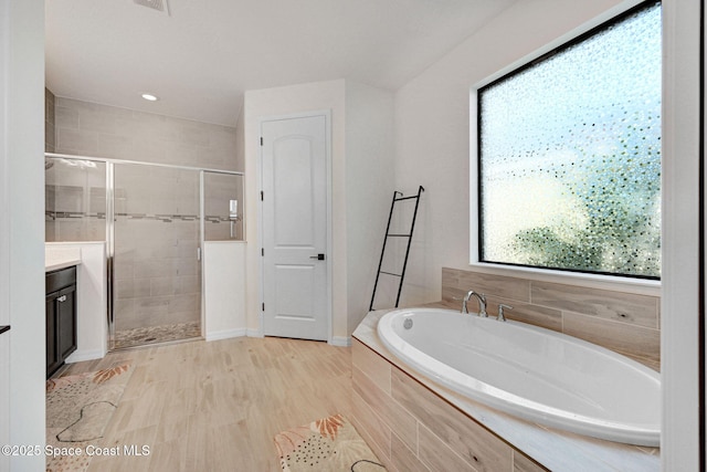 bathroom with wood finished floors, plenty of natural light, a garden tub, and a shower stall