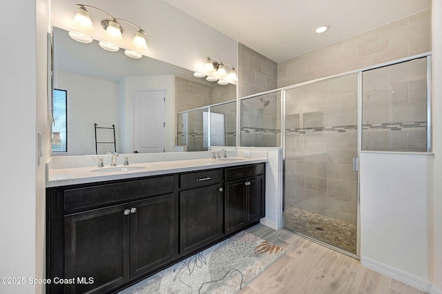 bathroom featuring a stall shower, double vanity, wood finished floors, and a sink
