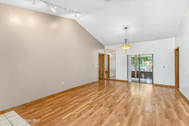 523 Hidden Hollow Dr, Merritt Island, FL 32952 - empty room with rail lighting, vaulted ceiling, light wood-type flooring, baseboards, and a textured ceiling