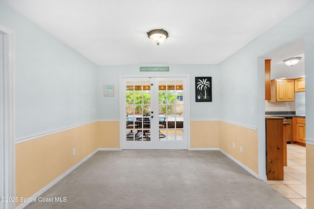 unfurnished room with baseboards, light carpet, a textured ceiling, and french doors