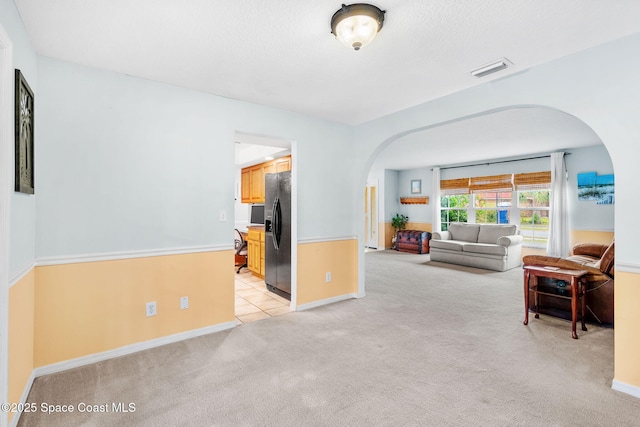 living room featuring arched walkways, visible vents, light carpet, and baseboards