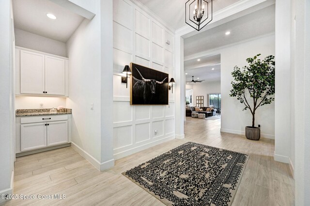 corridor with crown molding, recessed lighting, an inviting chandelier, baseboards, and light wood-style floors