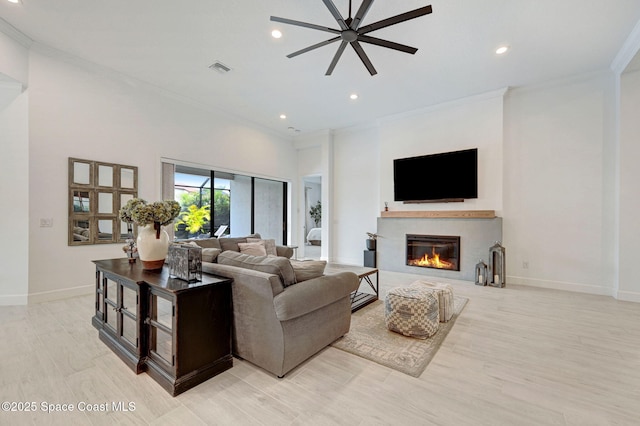 living area with recessed lighting, ornamental molding, baseboards, ceiling fan, and a glass covered fireplace