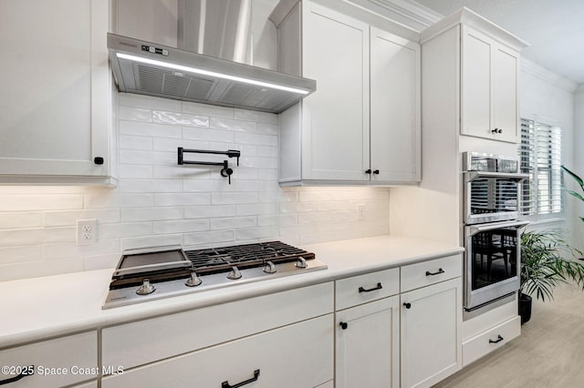 kitchen with light countertops, stainless steel appliances, range hood, and white cabinets