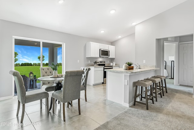 kitchen featuring light countertops, a peninsula, a kitchen bar, stainless steel appliances, and white cabinetry
