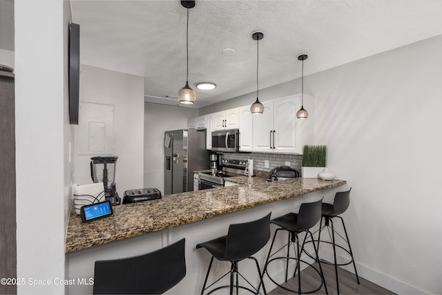 kitchen featuring stainless steel appliances, a breakfast bar, backsplash, dark stone counters, and white cabinets