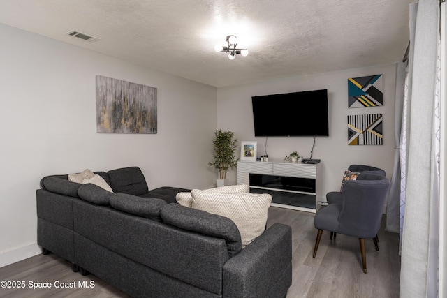 living area with baseboards, visible vents, a textured ceiling, and wood finished floors
