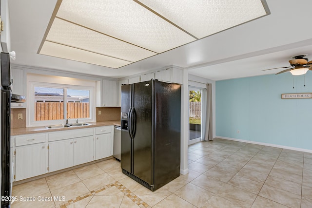 kitchen with light tile patterned flooring, light countertops, a sink, white cabinetry, and black fridge