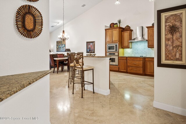 129 Lancha Cir Unit 201, Indian Harbour Beach, FL 32937 - kitchen featuring a kitchen bar, tasteful backsplash, wall chimney exhaust hood, stainless steel appliances, and brown cabinets