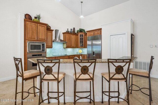 129 Lancha Cir Unit 201, Indian Harbour Beach, FL 32937 - kitchen with wall chimney exhaust hood, a breakfast bar, backsplash, built in appliances, and brown cabinets