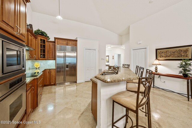 129 Lancha Cir Unit 201, Indian Harbour Beach, FL 32937 - kitchen featuring light stone counters, a sink, built in appliances, a kitchen bar, and brown cabinetry