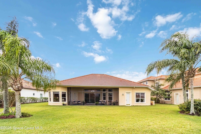 back of house featuring a sunroom, stucco siding, a tile roof, and a lawn