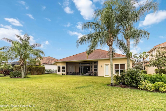 rear view of property featuring a sunroom, a tiled roof, stucco siding, and a lawn
