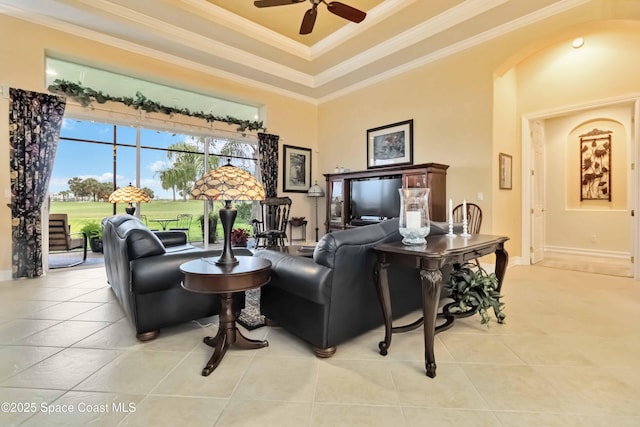 living area with baseboards, tile patterned flooring, a ceiling fan, crown molding, and a tray ceiling