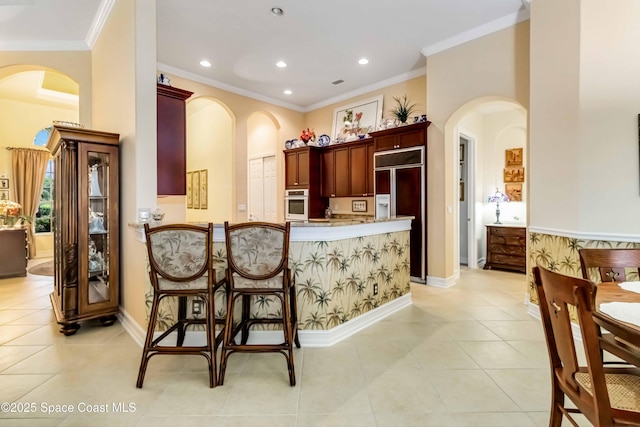 kitchen featuring crown molding, dark brown cabinets, paneled built in fridge, stainless steel oven, and arched walkways