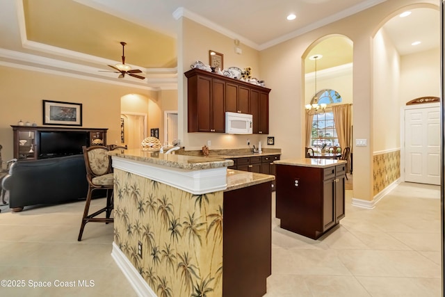 kitchen featuring light tile patterned floors, arched walkways, ornamental molding, white microwave, and a kitchen island